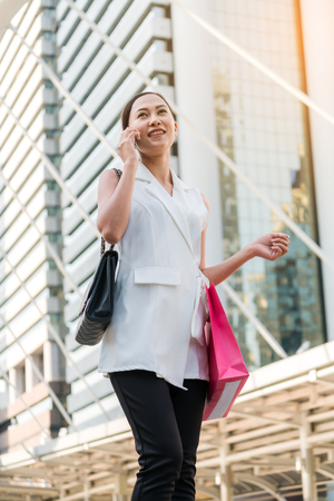 Woman talking on phone, holding shopping bags in modern city background. Woman lifestyle and shopping concept.の写真素材