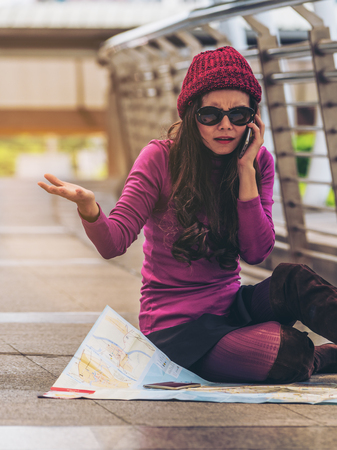 Lost woman traveller making phone call asking for help while looking at the map. Travel problem and lost concept. Travel lifestyle.の写真素材