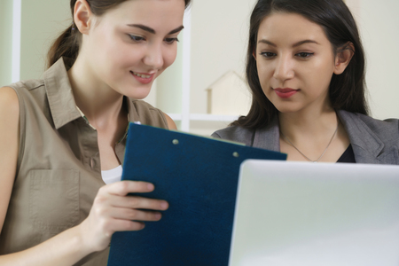 A business woman works in office while having a business conversation with another woman. Concept of co-working business partner and friends in workplace.の写真素材