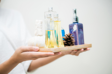 Woman holding spa treatment set including aromatic massage oil, body scrub lotion and herbal spa compress while wearing a bathroom suit.の写真素材