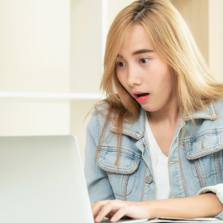 Cute woman feels amazed, excited or surprised while looking at laptop computer in cozy home office....