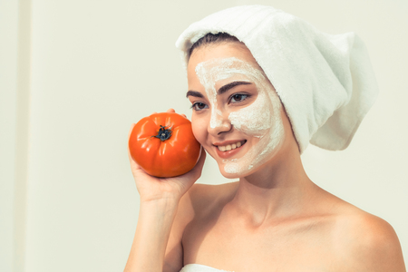 Beautiful woman having a facial mask treatment with tomato cream extract showing benefit of nature treatment. Anti-aging cosmetology, facial skin care and luxury lifestyle concept.の写真素材