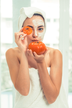 Beautiful woman having a facial mask treatment with tomato cream extract showing benefit of nature treatment. Anti-aging cosmetology, facial skin care and luxury lifestyle concept.の写真素材
