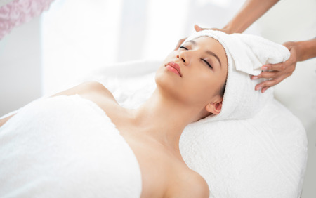 Relaxed young woman lying on spa bed prepared for facial treatment and massage in luxury spa resort. Wellness, stress relief and rejuvenation concept.の写真素材