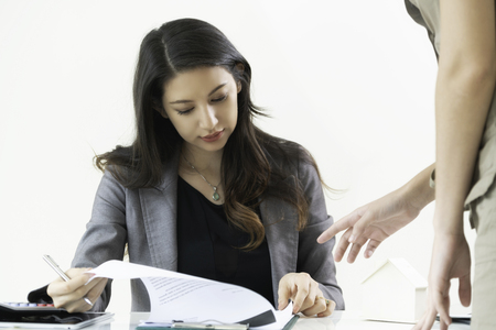 Businesswoman reads paper documents while discussing with another businesswoman standing in front of her partner at the office.の写真素材