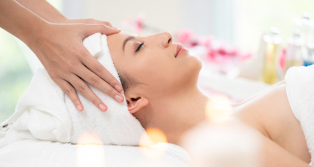 Relaxed woman lying on spa bed for facial and head massage spa treatment by massage therapist in a luxury spa resort. Wellness, stress relief and rejuvenation concept.の写真素材