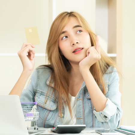 Beautiful woman holding credit card at home and thinking about shopping on the online stores. Concept of modern online shopping.の写真素材