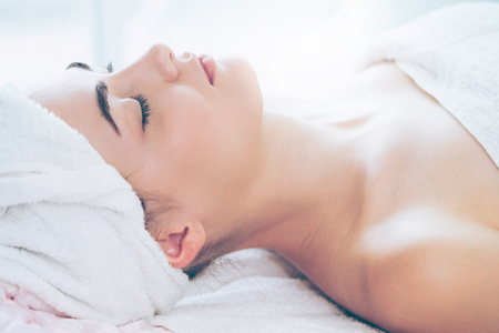 Relaxed young woman lying on spa bed prepared for facial treatment and massage in luxury spa resort. Wellness, stress relief and rejuvenation concept.の写真素材