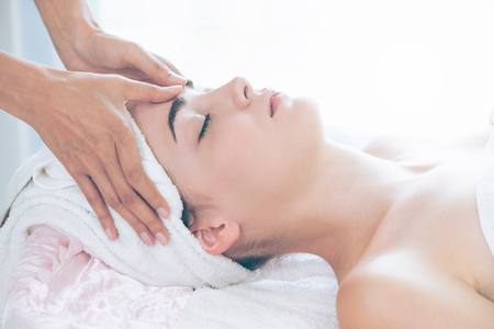 Relaxed woman lying on spa bed for facial and head massage spa treatment by massage therapist in a luxury spa resort. Wellness, stress relief and rejuvenation concept.の写真素材