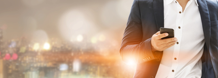 Young businessman using mobile phone with modern city buildings background. Future telecommunication technology and internet of things ( IOT ) concept.の写真素材