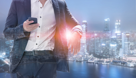Young businessman using mobile phone with modern city buildings background. Future telecommunication technology and internet of things ( IOT ) concept.の写真素材