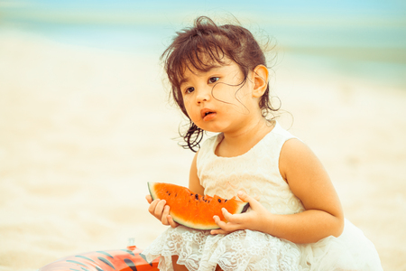 Adorable kid eating watermelon on the tropical sand beach in summer.の写真素材