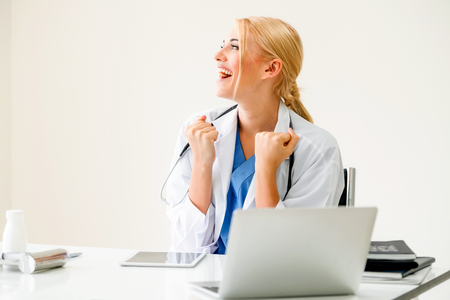 Happy successful woman doctor feels delightful in hospital or healthcare institute while working on medical report at office table. Success concept.の写真素材