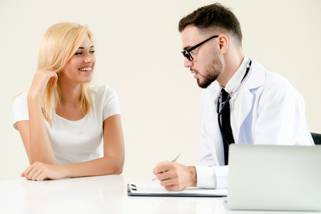 Male doctor talks to female patient in hospital office while writing on the patients health record on the table. Healthcare and medical service.の写真素材