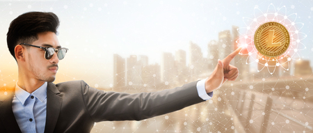 Litecoin and cryptocurrency investing concept - Businessman pointing at Litecoin (LTC) with modern business building and cityscape in the background. Blockchain technology.の写真素材