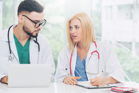 Young female doctor works at office in hospital while talking to male doctor sitting beside her. Medical service and healthcare concept.の写真素材