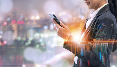 Young businesswoman using mobile phone with modern city buildings background. Future telecommunication technology and internet of things ( IOT ) concept.の写真素材