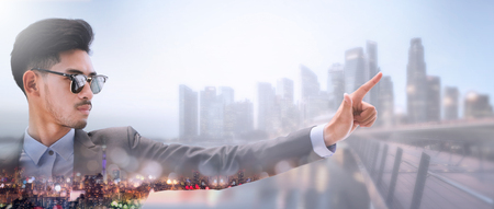 Businessman pointing finger at copy space for your business text or logo with modern city in background. Double exposure image.の写真素材