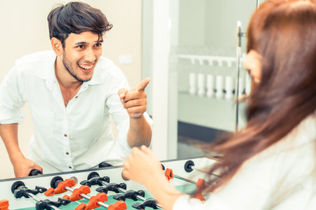 Happy young man playing foosball table soccer with girlfriend. Couple recreation and lifestyle.
