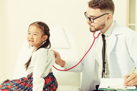 Young male doctor examining little kid in hospital office. The kid is happy and not afraid of the doctor. Medical children healthcare concept.の写真素材