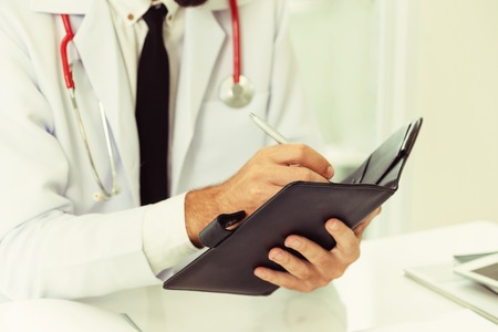 Doctor reading while writing note on a book at office in the hospital. Medical and healthcare concept.の写真素材