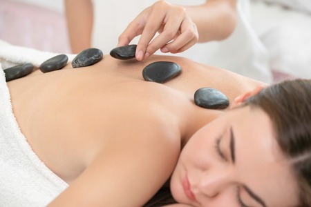 Woman getting hot stone massage treatment by professional beautician therapist in spa salon. Luxury wellness, back stress relief and rejuvenation concept.の写真素材