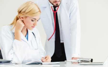 Doctor at hospital office writes notes on patients report while having conversation with another doctor that standing beside her.の写真素材