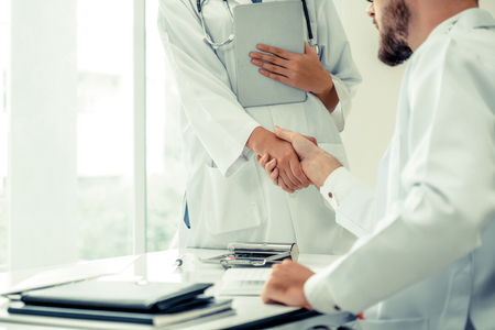 Doctor at the hospital giving handshake to another doctor showing success and teamwork of professional healthcare staff.の写真素材