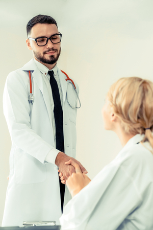 Doctor at the hospital giving handshake to another doctor showing success and teamwork of professional healthcare staff.の写真素材