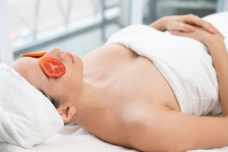 Relaxed young woman getting eye nature treatment by tomato at luxury spa resort. Wellness and healing concept.の写真素材