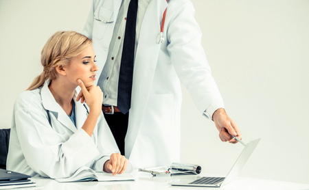 Doctor at hospital office working on laptop computer on the table with another doctor having discussion about patients health.の写真素材