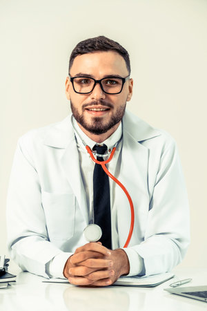 Happy male doctor at office desk in hospital working on laptop computer. Medical healthcare concept.の写真素材