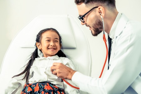 Young male doctor examining little kid in hospital office. The kid is happy and not afraid of the doctor. Medical children healthcare concept.の写真素材