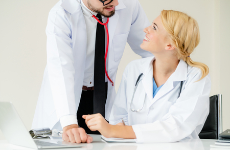 Doctor at hospital office writes notes on patients report while having conversation with another doctor that standing beside her.の写真素材