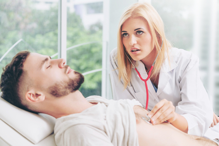 Woman doctor is talking and examining male patient in hospital office. Healthcare and medical service.の写真素材