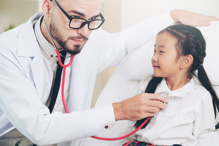 Young male doctor examining little kid in hospital office.の写真素材
