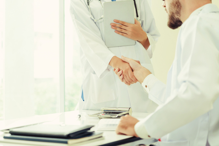 Doctor at the hospital giving handshake to another doctor showing success and teamwork of professional healthcare staff.の写真素材