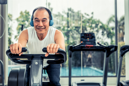Senior man exercise on cycling machine in fitness center. Mature healthy lifestyle.の写真素材