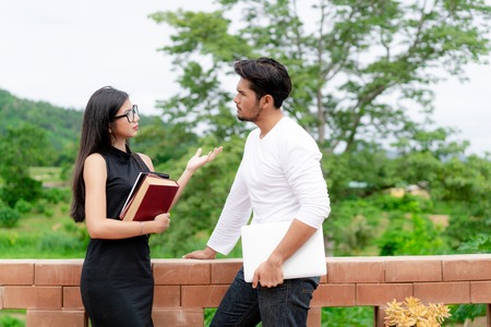 Two students with books and laptop talking in the university. College education concept.の写真素材