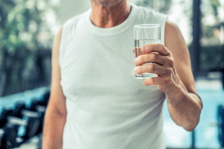 Senior man drink mineral water in gym fitness center after exercise. Elderly healthy lifestyle.