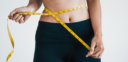 Close up shot of woman with slim body measuring her waistline and torso. Healthy nutrition and weight losing concept.の写真素材