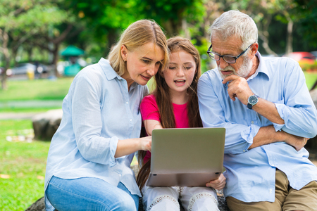 Happy family using laptop computer together in the garden park in summer. Kid education and family activities concept.の写真素材