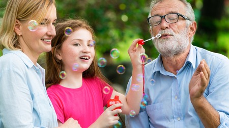 Happy family blows soap bubbles together while going vacation on weekend in the garden park in summer. Kid education and family activities concept.の写真素材