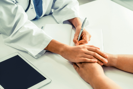 Woman doctor holds patient hand patient in room of hospital office. Healthcare and medical service.の写真素材
