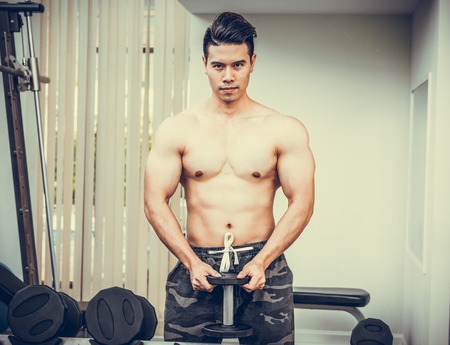 Muscular man bodybuilder in fitness gym training with dumbbells. Healthy lifestyle and bodybuilding concept.の写真素材