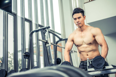 Muscular man bodybuilder in fitness gym training with dumbbells. Healthy lifestyle and bodybuilding concept.の写真素材