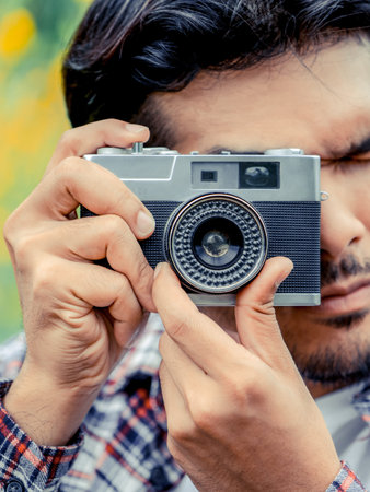 Young hipster man taking photo with old style camera with nature landscape background. Retro and...