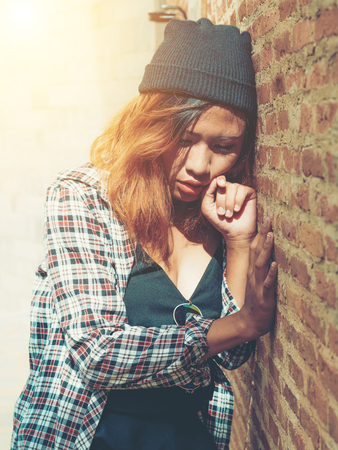 Depressed teenage woman feeling sad alone against brick wall in old town. Education and family failure concept.の写真素材