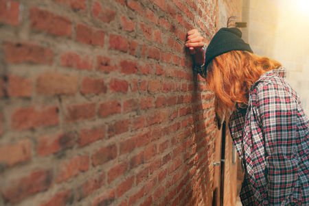 Depressed teenage woman feeling sad alone against brick wall in old town. Education and family failure concept.の写真素材