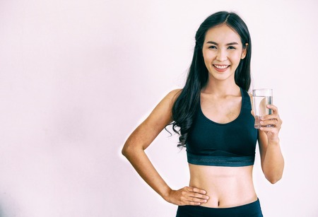 Woman in sportswear drinking water in a fitness gym. Healthy lifestyle and hydration concept.の写真素材